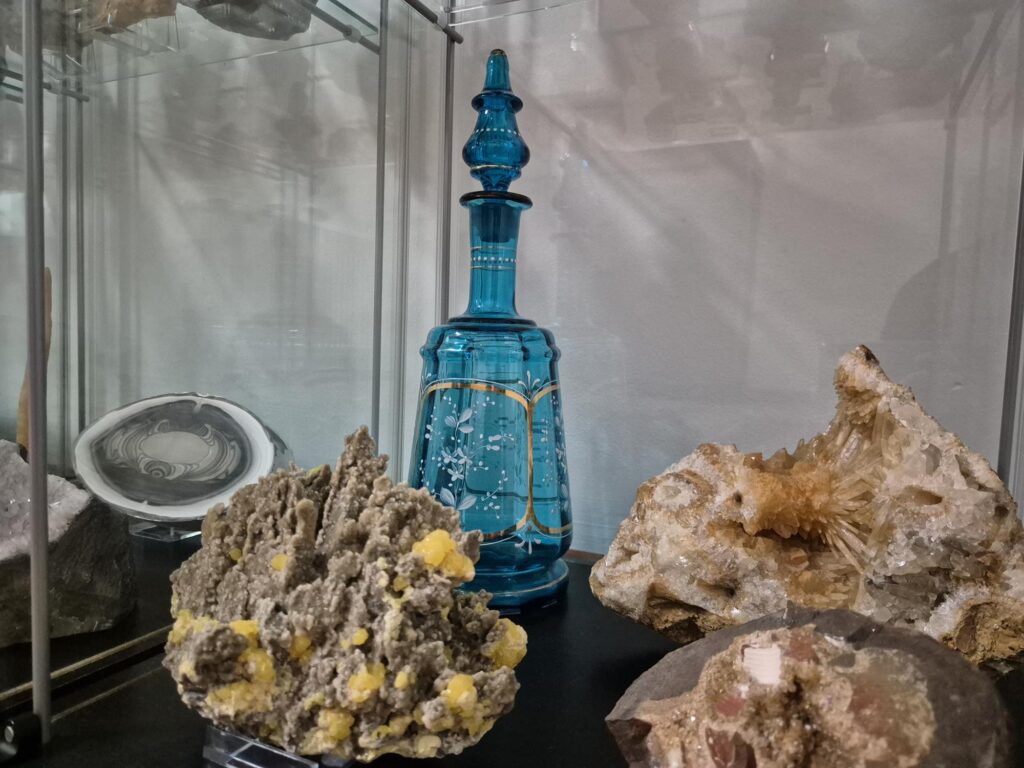 Kolekcja minerałów z szklaną karafką w tle. Szkło minerały w porównaniu z przedmiotami takimi jak szkło użytkowe